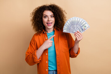 Photo portrait of lovely young lady point excited money banknotes dressed stylish orange garment isolated on beige color background
