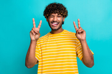 Photo of excited crazy young man eye wink tongue out demonstrate v-sign isolated on teal color...