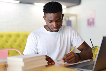 Serious young man, a student, sitting at a desk in a university setting, studying with a laptop and books.