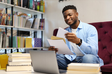 Serious young man in a library, studying with a laptop, embodying modern education and business knowledge. - obrazy, fototapety, plakaty
