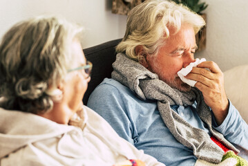 Couple old aged senior people at home with seasonal winter cold illness disease  sit down on the...