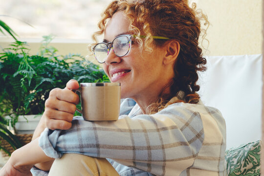 Adult Woman Smile Sitting On The Lounge Chair And Have Relax Time Drinking Cup Of Coffee Or Tea. Happy Relaxed Lifestyle For Female People With Eyeglasses