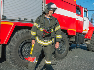 A firefighter in protective clothing and helmet holds an assault axe in his hands. A firefighter...