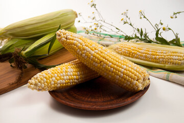 Clay plate with two cobs sweet corn on white wooden background..