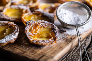 Mini tarts made of puff pastry and sliced apples sprinkled with powdered sugar on wooden cutting board