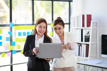 Smiling businesswoman discussing with colleague over laptop at desk in office