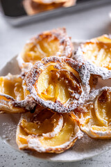 Mini tarts made of puff pastry and sliced apples sprinkled with powdered sugar on white plate