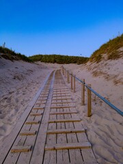 Vertical shot of the wooden stairs at the beach surrounded by small green hills at sunset