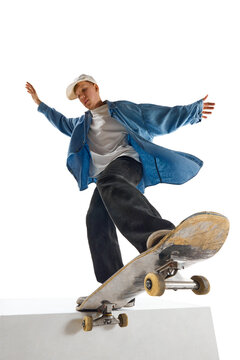 Dynamic image of teen boy in blue shirt and capo training, in motion, skateboarding isolated over white background. Concept of professional sport, competition, training, action. Copy space for ad