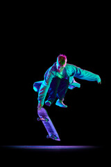 Dynamic image of young man in casual clothes in motion, training, skateboarding against black studio background in neon light. Concept of professional sport, competition, training, action.