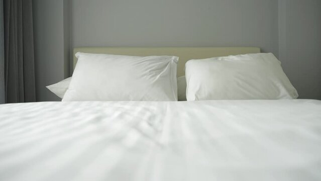 Close up of empty twisted bed with white bedding sheet near the window at day in the bedroom of the apartment. Calm sleep and relaxation at home