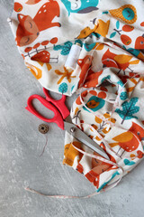Sewing tools: scissors, thread, fabric, pins, buttons and colorful soft cotton fabric on grey background with copy space Flat lay composition with sewing accessories 