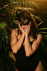 Sexy woman in a BDSM cat mask posing in a tropical garden among palm trees. BDSM concept.