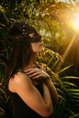 Sexy woman in a BDSM cat mask posing in a tropical garden among palm trees. BDSM concept.