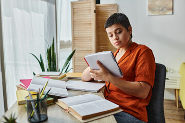 attractive young student looking attentively at her notes sitting at desk, education at home