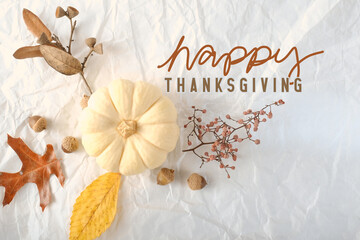 Happy thanksgiving greeting with flat lay of pumpkin and autumn leaves on white texture background.
