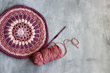Pink and purple round crochet pattern on light grey textured background with copy space. Close up photo of hand made trivet or potholder. 