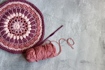 Crocheted trivet made of pink organic yarn. Handmade crochet potholder on gray background with...
