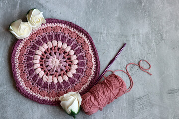 Crocheted trivet made of pink organic yarn. Handmade crochet potholder on gray background with space for text. 
