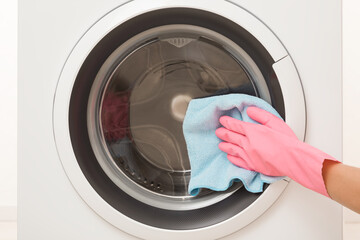 Woman hand in pink rubber protective glove using blue dry rag and wiping glass door surface outside...