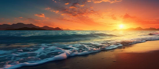 Foto op Plexiglas Strand zonsondergang The beautiful sunset paints the sky with shades of orange and blue creating a breathtaking backdrop for the beach as gentle waves kiss the shore and the warm summer sun bathes the landscape