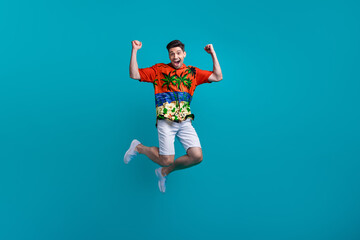 Obraz premium Full body photo of funky jumping crazy guy fists wear tropics shirt celebrate summertime season hooray isolated on blue color background