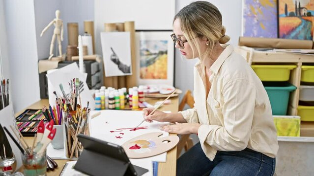 Young blonde woman artist drawing on paper using touchpad at art studio