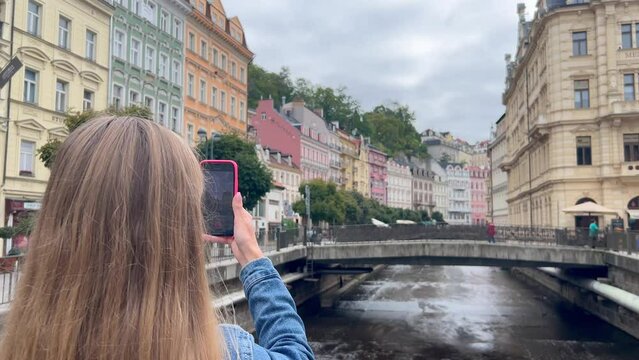A young woman looking at the scenery of the old city and taking photos on a smartphone. Travels in Europe
