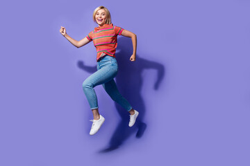 Fototapeta na wymiar Full length photo of funny young blonde bob hair lady run wear striped t shirt denim jeans white sneakers isolated on violet color background