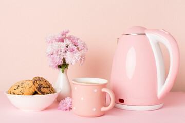 Pink electric kettle with cup of tea and dessert on table
