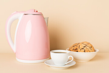 Pink electric kettle with cup of coffee and dessert on table