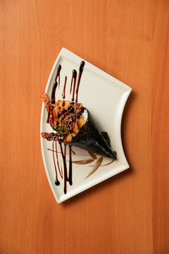 temaki de camar&atilde;o empanado com arroz, enrolado em uma nori, coberto por cebolinha e cream cheese, coberto com molho tar&ecirc;, em um prato de cer&acirc;mica e wallpaper