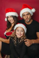 Beautiful family wearing Santa hat on red background