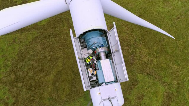 Anonymous man working on wind turbine. Aerial top down view of windmill farm for energy production on beautiful cloudy sky in highlands.