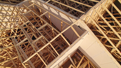 Housing gables roof on wood sticks. Wooden city home under construction at golden hour. New downtown building roof with wooden truss beam framework.