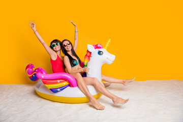 Photo of positive cheerful girls swim sand on rubber pony horse enjoy summer resort isolated bright...