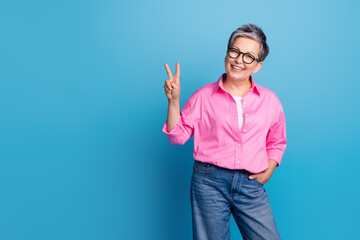 Portrait of cheerful person with white grey hairdo wear stylish blouse in eyewear showing v-sign isolated on blue color background