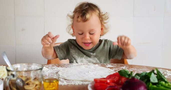 A joyful baby boy becomes adorable kitchen helper, playfully scattering pinch of flour onto pizza flatbread. Heartwarming scene of his cheerful exploration and bonding moment with his mother