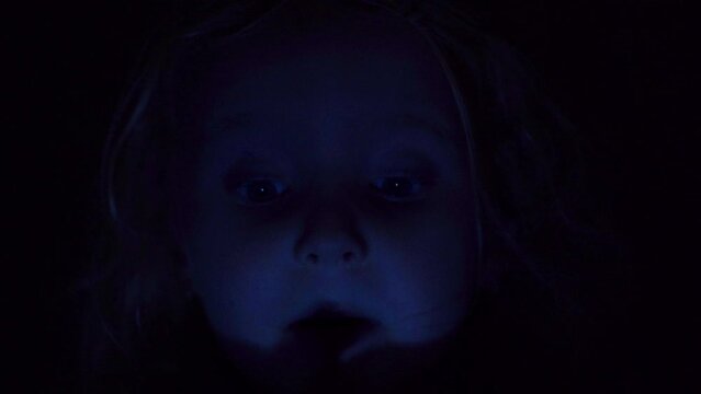 the child's face is in the dark and the light is flashing,little girl talking in the dark, night shot of face close-up