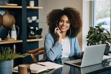 Obraz premium African American Female entrepreneur talking over mobile phone and looking at camera while working over laptop at home