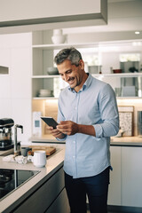 Happy businessman discussing financial report over smart phone while standing at kitchen counter