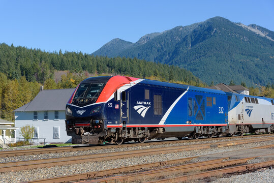 Skykomish, WA, USA - October 28, 2023; Amtrak ALC-42 Charger leads Empire builder train past Cascade Mountains in rural Washington State with full length train and comparison of locomotive styles
