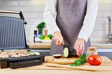 Female chef cuts vegetables and eggplants on a wooden cutting board. Cooking in the home kitchen.