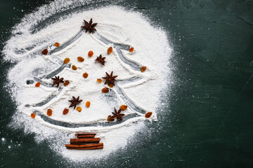 Christmas tree with star of anise, sultans or yellow raisins, and cinnamon bark on a white flour over green background. Table top view - obrazy, fototapety, plakaty