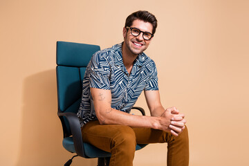 Photo of young cheerful team leader sitting boss armchair waiting for interview with new candidates isolated on beige color background