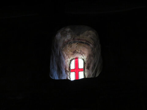 Colorful glass window of white and ress cross in darkness of cave church
