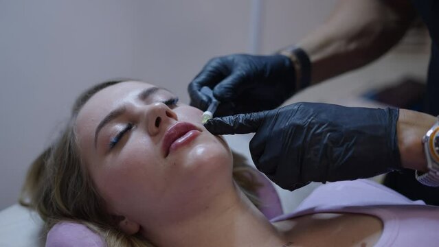 Doctors hands injecting hyaluronic acid into patients cheek