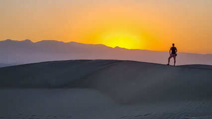 Silhouette of man enjoying the sunrise with scenic view on Mesquite Flat Sand Dunes, Death Valley...
