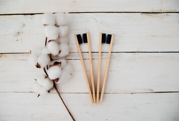 Eco-friendly bamboo toothbrushes and cotton flowers on a wooden background. Zero waste. The concept of natural organic cosmetics for the bathroom.