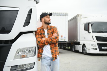 Portrait of young bearded man standing by his truck. Professional truck driver standing by semi truck vehicle.